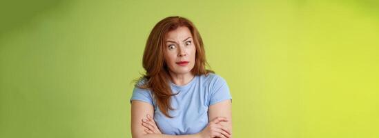 You did what. Confused shocked speechless redhead mature mother stare camera puzzled concerned cross arms chest self-soothing bothered pose look questioned hesitant green background photo