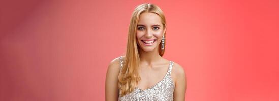 Charming glamour fabulous adult 25s blond woman in elegant silver dress shiny earrings smiling happily take part interesting conversation talking look friendly grinning, standing red background photo