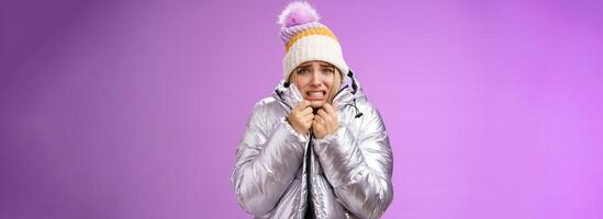 Uncomfortable shaking displeased charming gloomy blond cute woman in silver stylish jacket pulling coat tight wear hat shaking clenching teeth grimacing suffering low temperature freezing cold photo