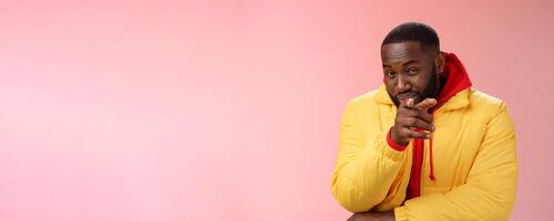 Guy suspecting you pointing camera index finger squinting disbelief unsure, standing pink background asking question look doubtful hesitant, express distrust wear yellow jacket red hoodie photo