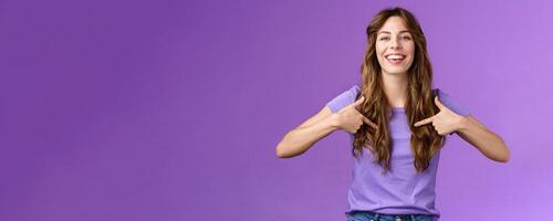 Boastful good-looking curly european female pointing herself proud who she is grinning delighted coming out pride month smiling broadly indicating center chest bragging purple background photo