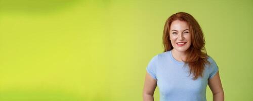 Cheerful kind happy redhead middle-aged mother look caring delighted smiling broadly gaze admiration joy stand blue t-shirt green background amused enthusiastic expression photo