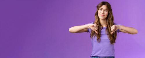 Disappointed displeased pity girl show thumbs down grimace dislike express negative opinion thumbs down gesture apologizing giving bad feedback stand purple background unimpressed photo