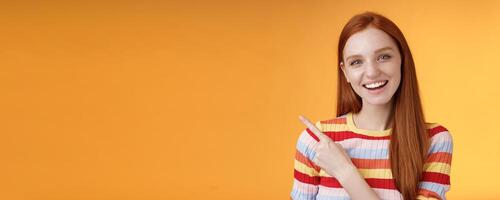 Friendly outgoing good-looking ginger girl university student discussing lecture classmate smiling laughing pointing upper left corner questioned curious know details standing orange background photo