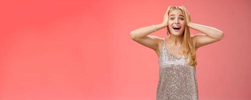 Amazed excited nervous young beautiful blond woman in silver stylish dress cannot believe own luck happiness hold hands head smiling screaming astonished positive awesome news, triumphing photo
