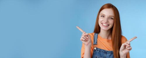 Friendly happy laughing pretty redhead girl female student showing lots opportunities advice make choice pointing sideways left right introducing different product grinning gladly, blue background photo