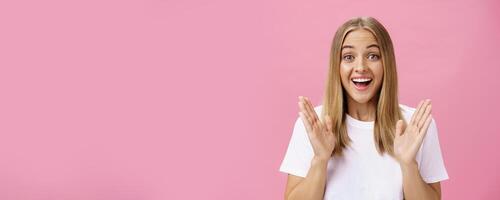 Woman learning awesome great news clasping hands in joy and excitement rejoicing feeling hapyp for friend smiling broadly and looking cheerful at camera with amused expression over pink background photo