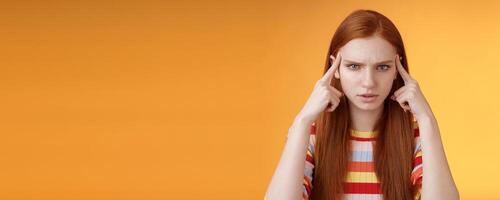 Puzzled serious-looking stressed-out young tired female student frowning look unhappy touching temples thinking trying focus, concentrate attention lecture memorizing hometask, orange background photo