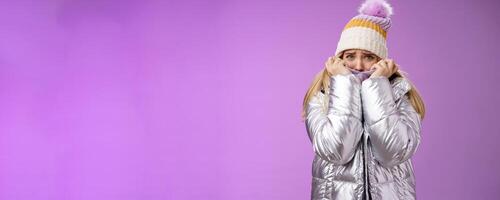 Scared afraid insecure coward girl in cute hat glittering shiny jacket pull cloth face frightened frowning stooping look concerned terrified scared death, standing purple background timid photo