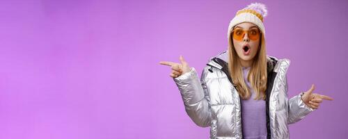 Impressed blond girl gasping widen eyes surprised folding lips wow sound check out incredible discounts winter equipment pointing left right cannot choose standing astonished purple background photo