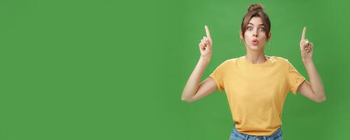 Authentic good-looking woman with natural beauty and tattoo on arm raising index fingers pointing up folding lips from interest and curiosity reacting impressed and excited at awesome advertisement photo