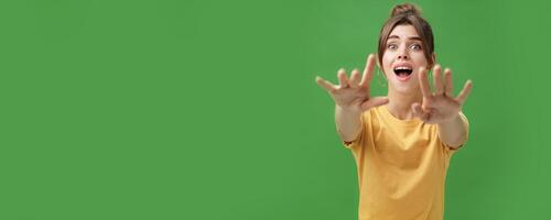 Excited and addicted goog-looking young woman reaching hands forward to camera with reckless look wanting grab something she desire seeing thing she wanted for long time over green background photo