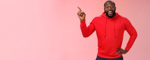 Enthusiastic happy good-looking young black guy beard pointing upper left corner smiling approval like curious about interesting item sale ask question excited impressed, standing pink background photo
