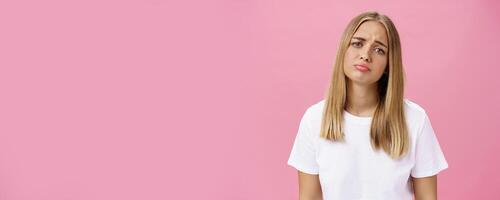 Sad girl whining tilting head raising eyebrows in upset expression and pursing lips feeling disappointed and envy, regretting missed chance standing unhappy and moody over pink background photo