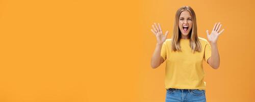 Woman releasing stress yelling with joy and pleasure gesturing with raised arms being daring and rebellious not afraid to show emotions standing passionate and expressive against orange background photo