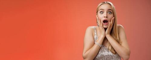 Shocked speechless concerned young stunned woman gasping screaming worried drop jaw touch cheeks widen eyes surprised nervously staring camera troubled afraid, standing red background photo