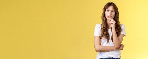 Troublesome situation give sec think. Intrigued thoughtful focused smart girlfriend thinking touch chin bite lip look camera focused pondering choice making decision solve problem yellow background photo