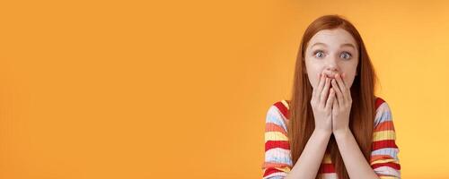 Excited shocked redhead speechless girl like gossiping standing emotional astonished hear amusing story gasping full disbelief cover mouth palm amazed posing orange background impressed photo