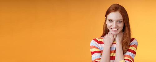 Pleased happy tender feminine redhead gorgeous girl blushing flirty giggle gazing camera smiling broadly touching neck modesy shy sensually talking guy likes standing orange background silly photo