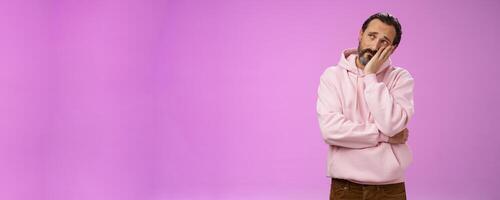 Sad gloomy bearded mature man lean head palm frowning look upper left corner thoughtful sorrow thinking bad times face hard problem standing upset disappointed down dumps, purple background photo
