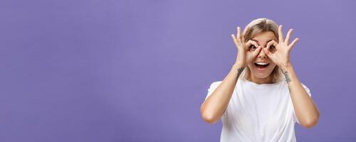Looking at awesome discounts. Portrait of impressed amused and happy good-looking stylish young woman with tattoos on arms making circles with hands over eyes smiling with admiration at camera photo