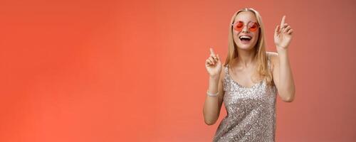 Amused attractive happy smiling woman dancing nightclub having fun enjoying go wild party celebrating b-day wearing stylish dress sunglasses raise index fingers smiling singing along photo
