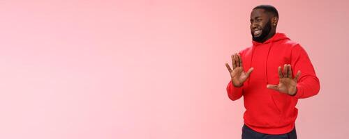 Awkward african american guy step back cringing dislike unwilling go party raise hands no thank stop refusal gesture smiling perplexed trying escape duties, standing bothered rejecting offer photo