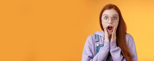 Shocked impressed redhead girlfriend drop jaw gasping screaming wow omg touch cheek near mouth wide eyes surprised reacting astonishing news fresh rumors gossiping amazed, orange background photo