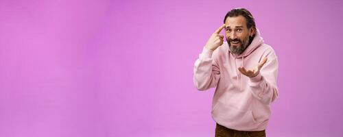 Outraged pissed man angry person crazy out of mind yelling bothered furiously gesturing rolling index finger temple accusing someone insane stupid, standing displeased intense purple background photo