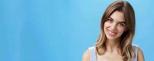Waist-up shot of charming self-assured authentic woman feeling great accepting own imperfections tilting head smiling broadly at camera and showing cute gapped teeth posing over blue background photo