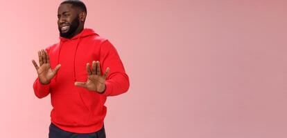 Awkward african american guy step back cringing dislike unwilling go party raise hands no thank stop refusal gesture smiling perplexed trying escape duties, standing bothered rejecting offer photo
