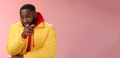 Guy suspecting you pointing camera index finger squinting disbelief unsure, standing pink background asking question look doubtful hesitant, express distrust wear yellow jacket red hoodie photo