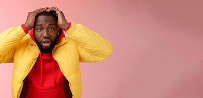Shocked stupefied young african-american bearded man grab head drop jaw gasping confused frustrated looking upset troubled have problems standing stunned concerned pink background photo
