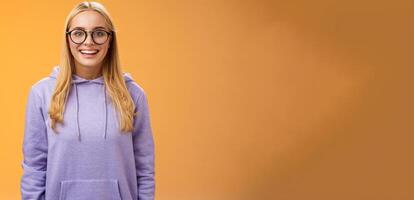 Charming female student geek smiling energized wanna participate university event grinning look excited wearing glasses purple hoodie standing amused orange background having fun photo