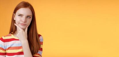 Hmm interesting. Suspicious doubtful attractive european redhead female pondering choice look hesitant thoughtful touch chin smirking tricky look upper left corner thinking, take decision photo