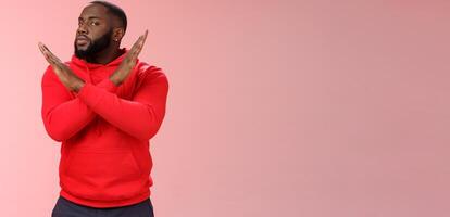 Cut it out. Portrait serious-looking african american male assisant show cross gesture say finish refusing, rejecting offer never gonna do it, standing reluctant pink background negative answer photo