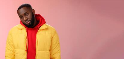 Unimpressed bored ignorant young african bearded man tilt head look scorn uninterest camera listen boring useless information, standing careless in yellow jacket red hoodie, indifferent photo
