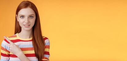Curious smart female redhead coworker asking friend who was that pointing left index finger look camera thoughtful questioned wanna know answer smiling intrigued standing orange background photo