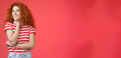 Cheerful lively cute tender redhead curly girl romantic summer mood pondering what present girlfriend happy pride month silly smiling touch face-line look curious camera red background photo