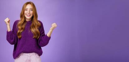 Girl proud of herself making successful effort clenching raised fists in celebration and triumph smiling broadly with surprised and relieved expression, winning, achieving goal over purple background photo