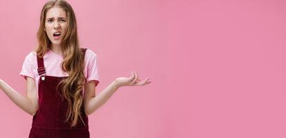 So what, no big deal. Rude and impolite arrogant young girl with high ego in overalls spreading hands sideways in questioned, bothered gesture expressing confusion, feeling pissed with stupid question photo