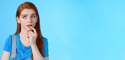Close-up curious dreamy creative redhead female working project, student thinking essay, touch lip intrigued, look up thoughtful, pondering choice, make assumptions, stand blue background photo