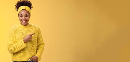Friendly ougoing relaxed african-american woman casually pointing right during conversation discussing recent new cafe open awesome discounts promos standing happily yellow background photo