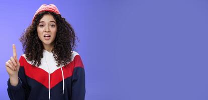 Rule number one do not mess with me babe. Portrait of swag and cool stylish young curly-haired woman in winter beanie showing index finger in prohibition or warning gesture over blue background photo