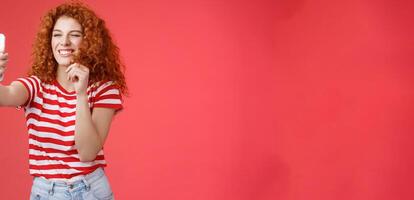 Sassy good-looking stylish charismatic redhead female curly hairstyle winking cheeky expression making flirty kinky faces hold smartphone taking selfie record message play funny facial filters photo