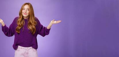 Well who cares, nothing to do. Portrait of funny and careless unbothered chill redhead female shrugging with spread hands and tight smile being unaware and not giving interest over purple background photo