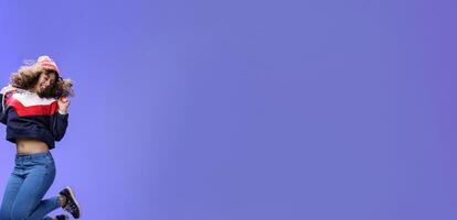 Girl jumping from happiness and delight feeling carefree close eyes and smiling broadly enjoying moment having fun raising hands being dreamy and playful over blue background photo
