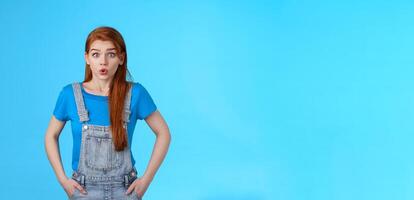 Worried nervous cute redhead female feel anxious pressured before important interview, hold breath, exhale, pouting difficult concerning situation, look insecure stand blue background photo