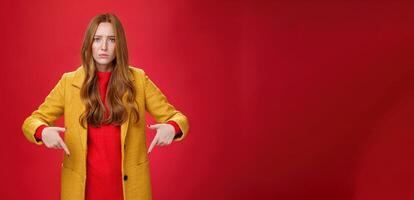 Portrait of sad and displeased moody girlfriend asking opinion with concerned upset expression pointing down looking focused and serious with unhappy face at camera over red background photo