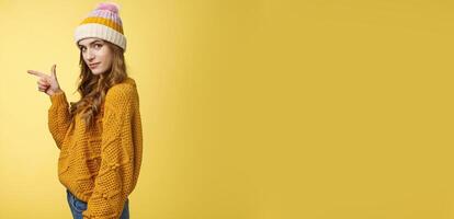 Profile shot confident flirty fashionable young 20s girl turning camera smiling pointing left inviting go together showing curious promotion cool place hang out, standing yellow background relaxed photo